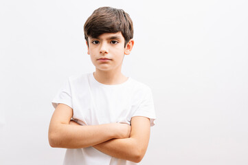 Beautiful kid boy wearing grey casual t-shirt standing over isolated white background face serious with crossed arms looking at the camera.