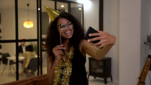 Pretty black girl taking a selfie and making funny faces at New Year's Eve party. Young african american woman celebrating Christmas at home. 