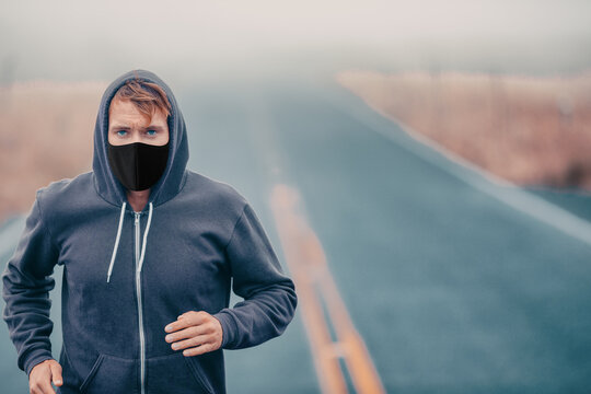 Sports mask endurance athlete runner running outside on road training while wearing facial covering in cold weather winter fog. Male jogger man jogging.