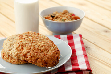 Oat cookies with oat flakes and cup of milk on wooden table
