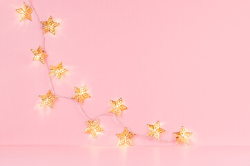 Christmas home interior with glowing golden stars garland on soft light pastel pink background,...