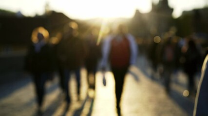 crowds of blurry local people and tourists wander along famous Charles Bridge with grey pavement under bright sunset light in spring evening 