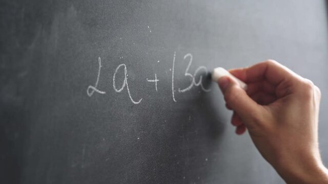 Woman's hand with chalk writes a formula on a blackboard