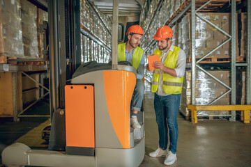 Two warehouse workers in helmets having a lively conversation