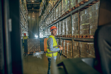 Worker in a vest and helmet standing in the warehouse and looking serious