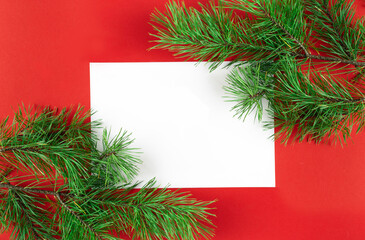 A frame of fir branches frames a white leaf on a red background. Christmas or New Year concept. Card. With space for text