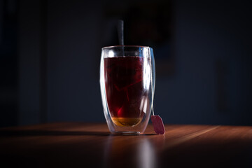 on a wooden plate stands one glass of tea with a tea bag inside and a spoon