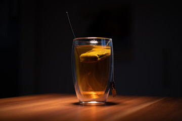 on a wooden plate stands one glass of tea with a tea bag inside and a spoon