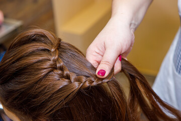 Naklejka premium Professional braiding of braids by a master hairdresser in a beauty salon. The concept of hair care.