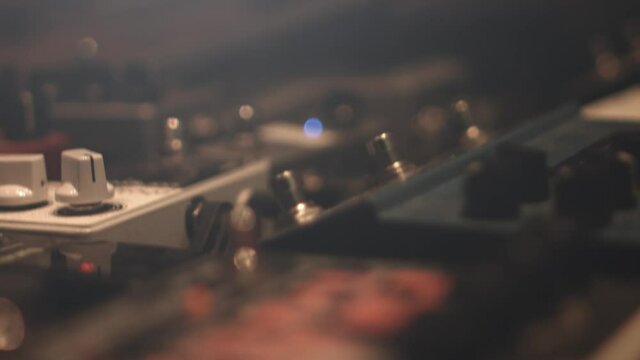 Close up of different guitar pedal effect stomp boxes on the floor in a recording studio with knobs and led indicator lights. Shot in 4K. Racking Focus with shallow depth of field.