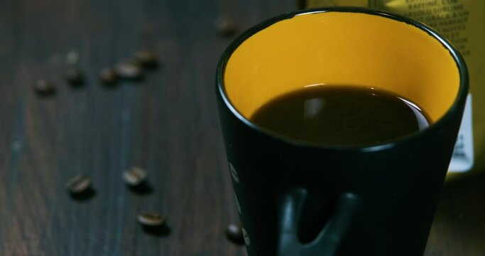 close up shot of a cup of coffee next to a packet of coffee beans and coffe beans on a wooden table