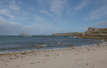 Fototapeta na wymiar Deserted Gimble Porth Beach with Round Island Lighthouse in the Distance and a Dramatic Cloudy Blue Sky Background on the Island of Tresco in the Isles of Scilly, England, UK