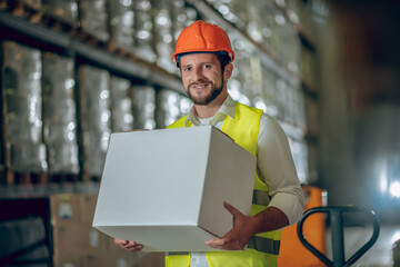 Young bearded worker carrying a box and smiling
