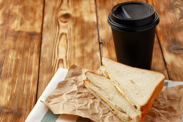 Toasted sandwich in craft paper with cup of coffee on table