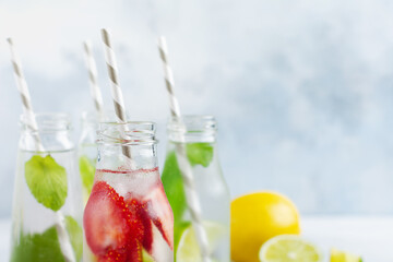 Lots of bottles with refreshing summer lemonade with lime, strawberry, cherry, cucumber and ice on a gray concrete background.