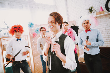 Men in wigs stand in a room as they celebrate.