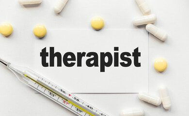 On white business card the inscription therapist in black letters. Near tablets and capsules....