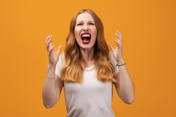 Angry young woman with wavy redhead, screaming on yellow studio background