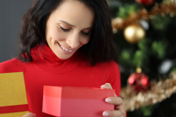 Young smiling woman looking into box with gift for new year. Christmas gifts concept