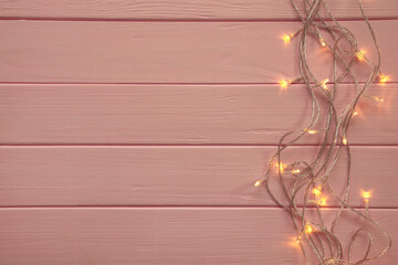Christmas garland lights on pink wooden background.