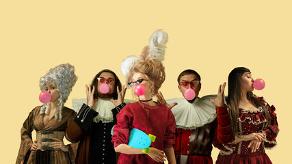 Medieval people as a royalty persons in vintage clothing blowing bubble gum on yellow background....