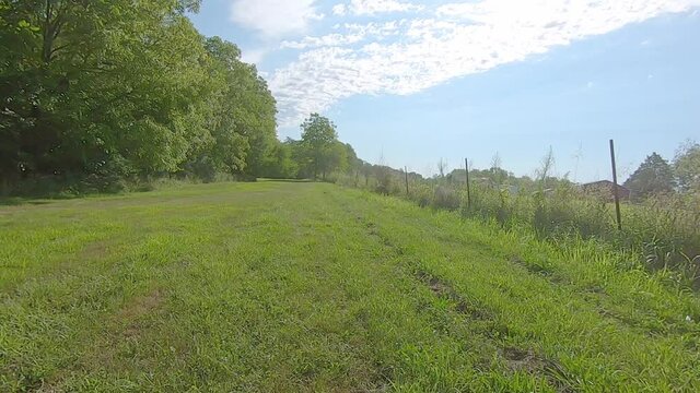 POV driving all-terrain vehicle in a wide grassy lane along fence row on a sunny afternoon