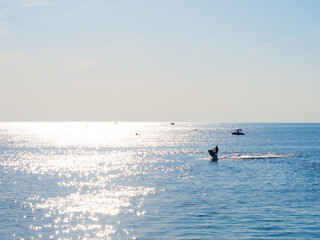Calm sea with sun glare path, scooter and boats in the distance