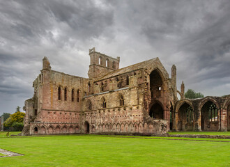 Landscape of the ruined medieval Melrose Abbey in Scotland, with very cloudy and gray sky.