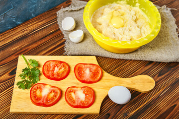 grated potato sliced red tomatoes two eggs on a wooden table. cooking potato pancakes