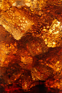 Cold carbonated drink over ice cubes in a glass close up