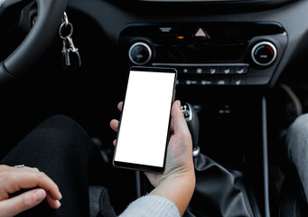 Young driver using smartphon in the car while driving or parking. Mockup of a mobile phone with isolated white screen in the hands of a woman.