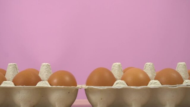 Open egg box with ten brown eggs on pink color background. Many fresh raw chicken eggs in cartons, dolly. Chicken brown fresh raw eggs in an egg container. Fresh organic chicken eggs in carton pack.