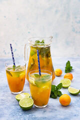 Homemade iced lemonade or tea with apricot, lime and mint. Fresh apricot mocktail in a jug and glasses on blue concrete background.