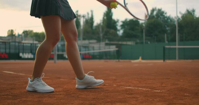 Slow motion close up: Young Caucasian teenager female tennis player serving during a game or practice. Tennis Player Serving On The Clay Court.