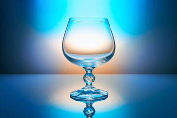 Empty cognac glass on beautiful color blue lighting background with reflection