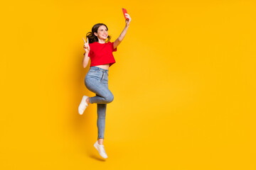 Fototapeta na wymiar Full body photo of girl jump take selfie smartphone make v-sign wear t-shirt jeans isolated shine color background