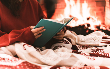 Female resting and warming up in a cold day covering with a blanket and reading a book - festive...