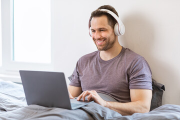 Man Using Laptop Wearing Headphones Watching Film Sitting In Bedroom