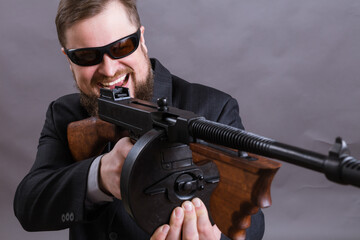 Mature man in sunglasses dressed in suit with tommy gun