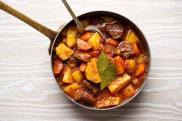 Delicious stew with meat, potatoes, carrot, herbs and gravy in rustic copper pot on white wooden...