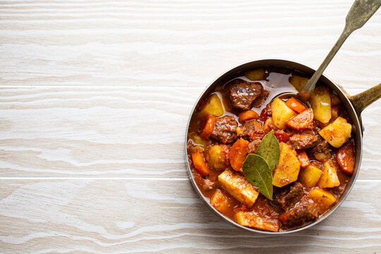 Delicious Stew With Meat, Potatoes, Carrot And Gravy In Rustic Copper Pot On White Wooden Background From Above. Traditional Winter And Autumn Dish Beef And Vegetables Ragout In Stewpot, Copy Space