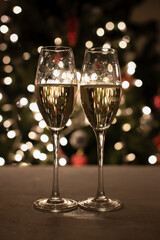 Sparkling wine in glasses against the background of a Christmas tree. Bokeh. Christmas together. Champagne in glasses. Vertical