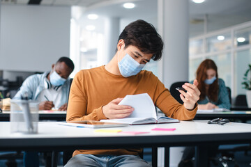 Asian male student in mask sitting at desk in class