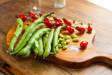 Assortment of beans and tomatoes with salt on a rustic wooden cutting board in natural light. Selective focus - shallow depth of field.