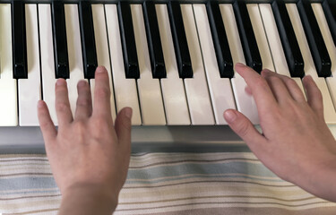 The hands of caucasian unrecognizable boy are learning to play synthesizer.