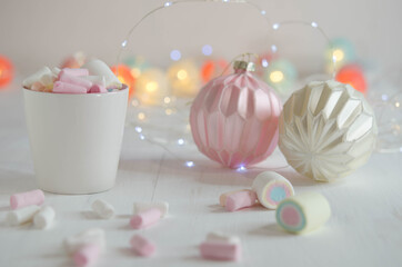 White cup with marshmallows and Christmas balls on a blurred background.