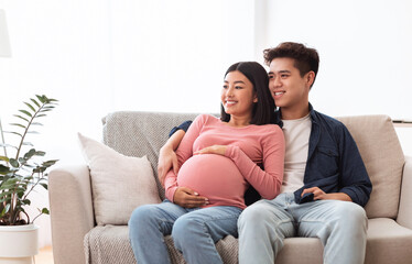 Asian Couple Watching TV Awaiting Baby Sitting At Home