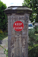 Fototapeta na wymiar Old Weathered Stone Gatepost with Red Metal 'Keep Clear' Sign