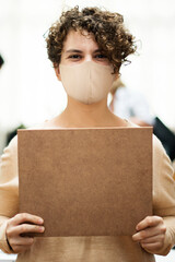 Woman wearing mask holding a blank placard in a shop