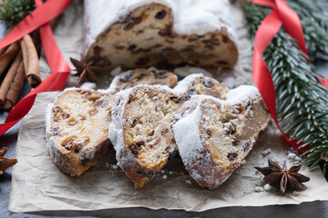 christmas cake with marzipan, nuts and raisins on parchment paper, spruce branches with red ribbons